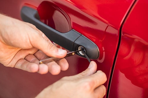 locksmith using lock pick tools on a car door lock